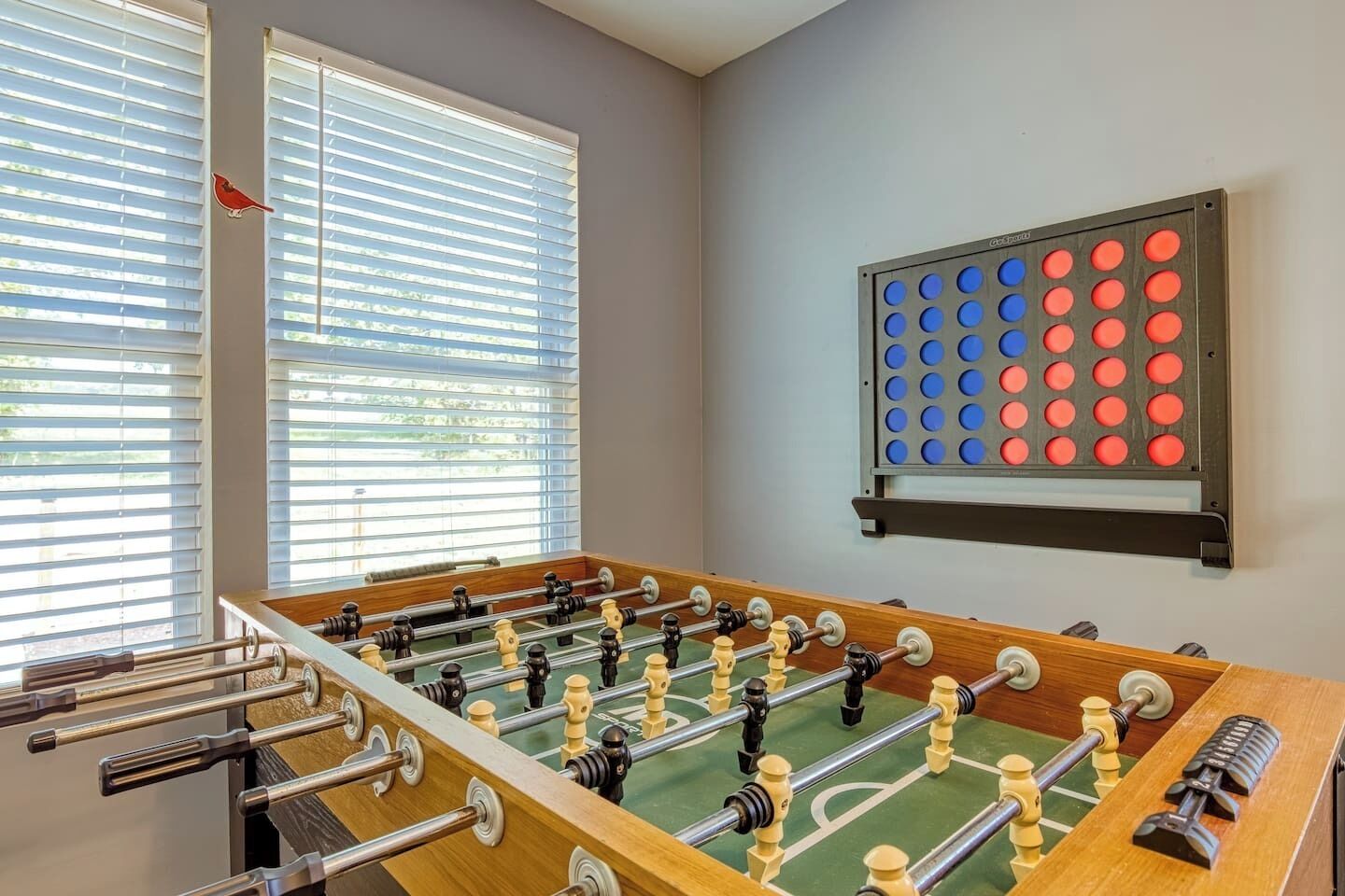 A foosball table in a room with large windows and a wall-mounted game board.