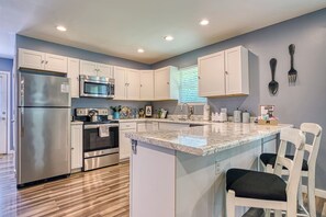 A modern kitchen with white cabinets, stainless steel appliances, a marble countertop, and a breakfast bar. - Sleepy Cub Hollow! Dollywood | Fenced In | Hot Tub (Sevierville)