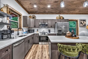 A modern kitchen with grey cabinets, stainless steel appliances, and a wooden ceiling. - The Woodland Reserve | Luxe Resort Cabin | Top 5%! (Sevierville)