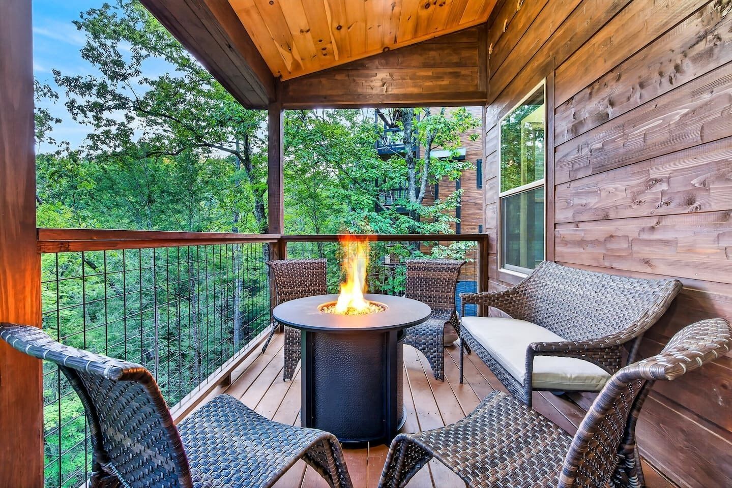 Une terrasse en bois avec une table ronde et des chaises, un foyer et une vue sur les arbres.