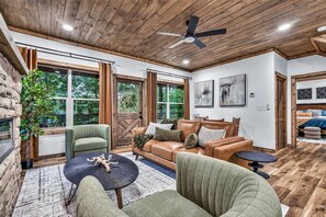A spacious living area with a wooden ceiling, large windows, a sofa, a coffee table, and a fireplace. - The Woodland Reserve | Luxe Resort Cabin | Top 5%! (Sevierville)
