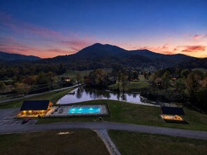 Une piscine dotée d’une zone couverte, entourée d’un parking et d’un petit bâtiment, avec une chaîne de montagnes en arrière-plan.