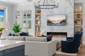 A modern living room with a fireplace, a large window, and a view of the outdoors. - NEW! Waterfront Luxury - Pool, Spa & Bay Views (Naples)