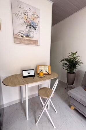 Ein zeitgemäßer Wohnraum mit einem weißen Tisch, einem Laptop, einer gelben Tasse, einer Topfpflanze und einem grauen Sofa.