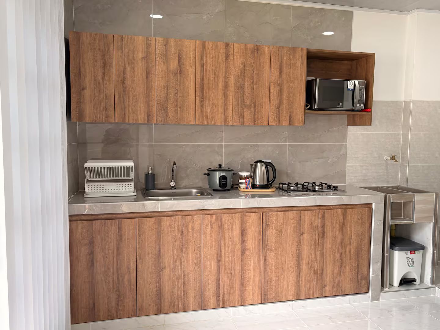 A modern kitchen with wooden cabinets, a microwave, a kettle, a toaster, and a gas stove.