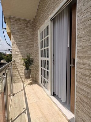 Uma varanda com parede de pedra, porta de correr de vidro e um vaso com planta.