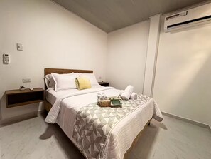 Ein Einzelbett mit einem geometrisch gemusterten Bettbezug, ein Nachttisch mit einer Pflanze und eine Wand-Klimaanlage.