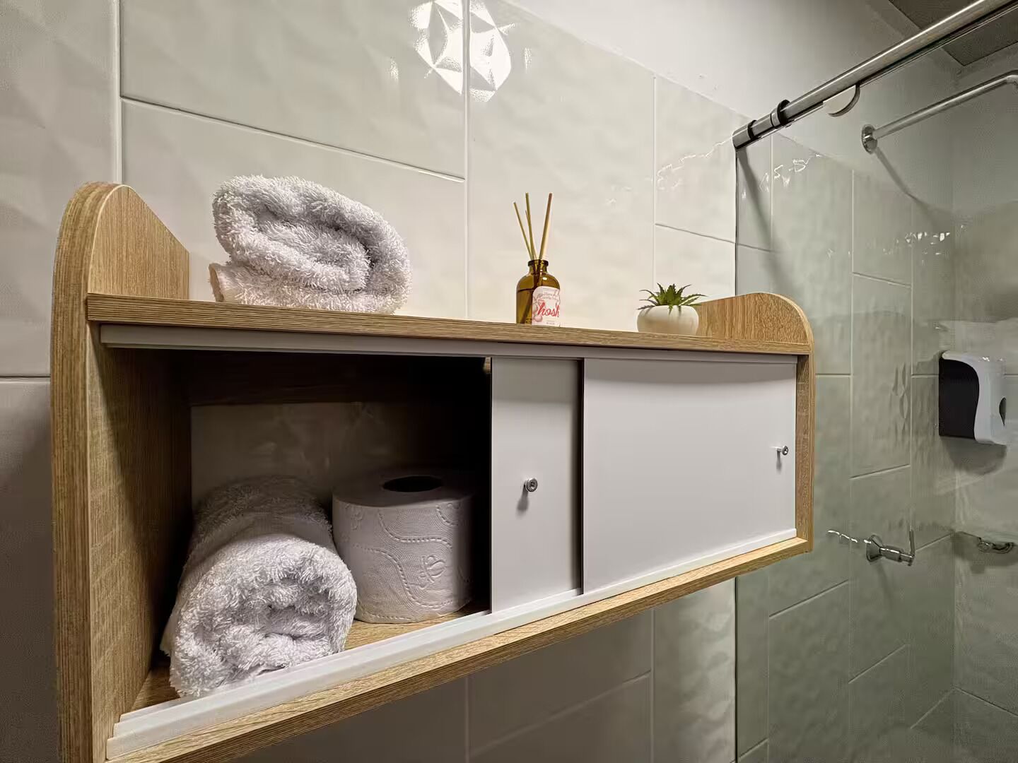 Une salle de bain avec un meuble-lavabo en bois, deux serviettes, un flacon de savon et une petite plante en pot.