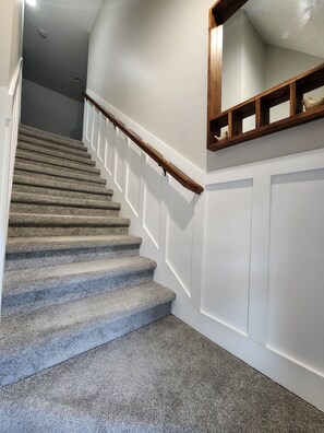 Eine mit Teppich ausgelegte Treppe mit weißer Wandverkleidung und einem Holzgeländer.