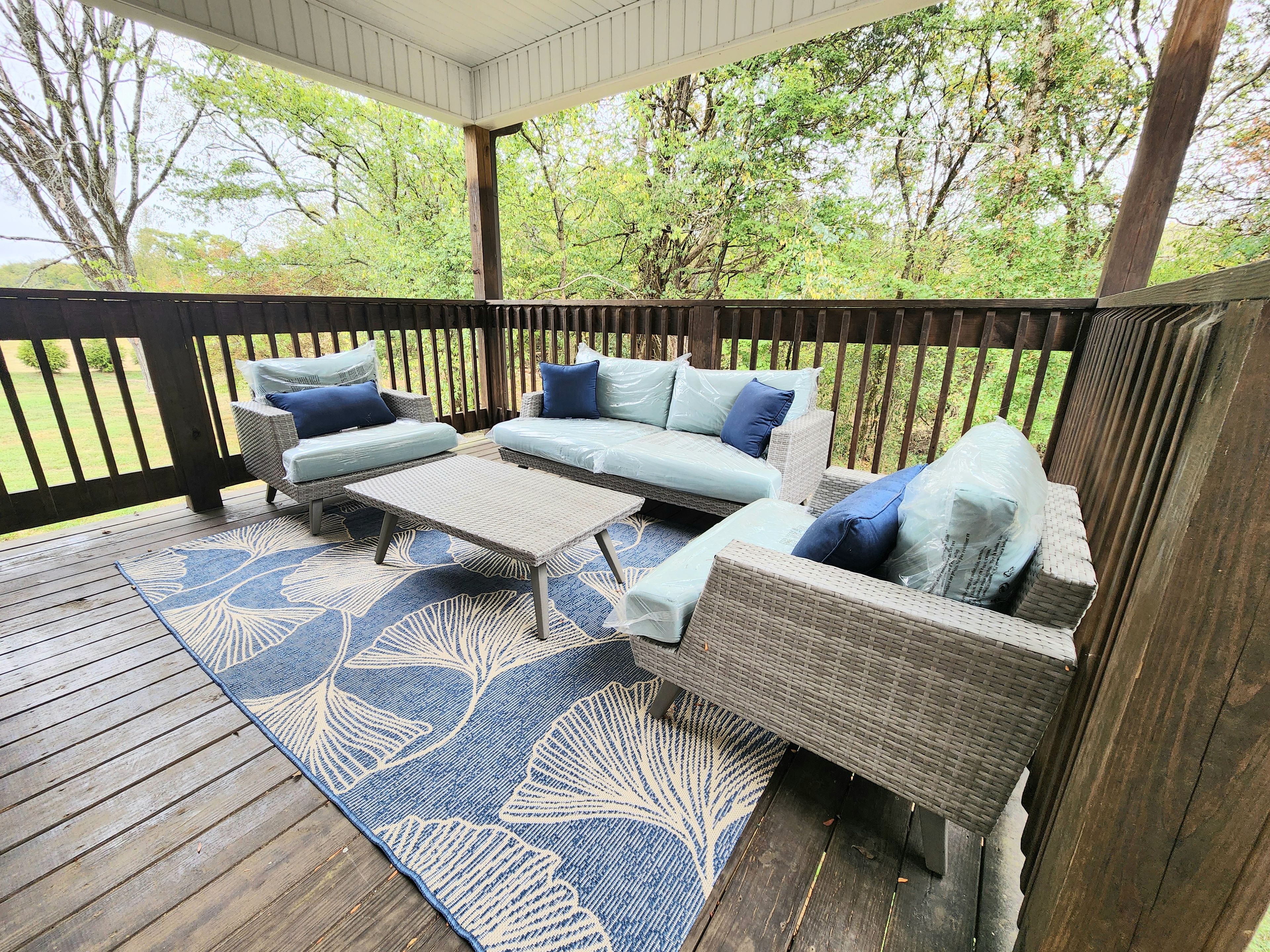 Een overdekt terras met rieten meubels en een blauw patroon tapijt.