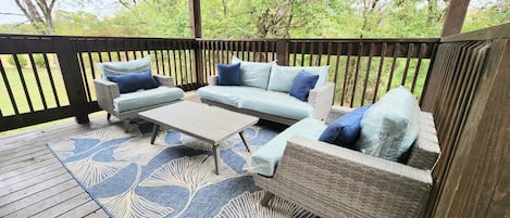 Een overdekt terras met rieten meubels en een blauw patroon tapijt.
