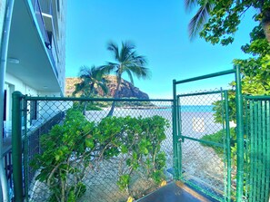 Un balcon avec vue sur la mer, un palmier et un immeuble doté d’un balcon.