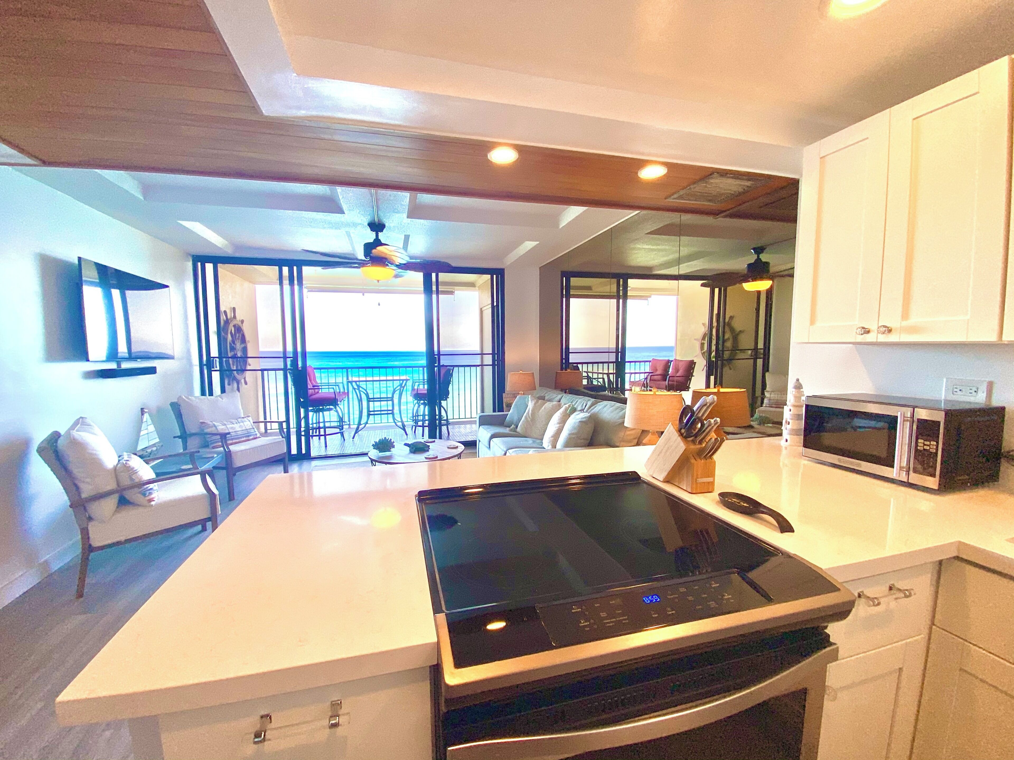 A modern kitchen with a central island, a microwave, and a dining area with a view of the ocean.