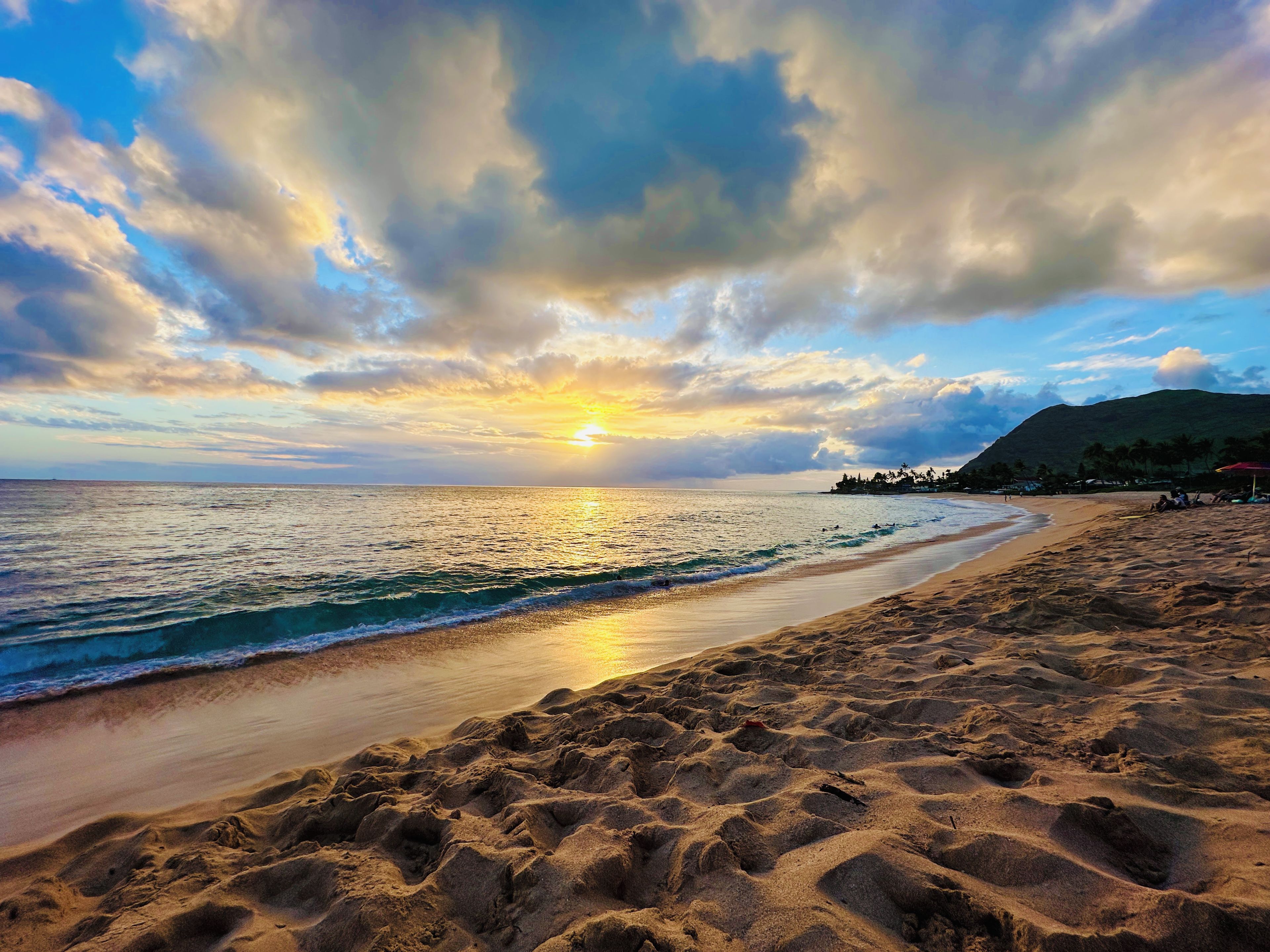 A beach with a sunset, waves, and a distant mountain.
