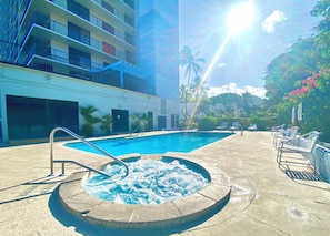 A swimming pool with a hot tub, lounge chairs, and a building with balconies.