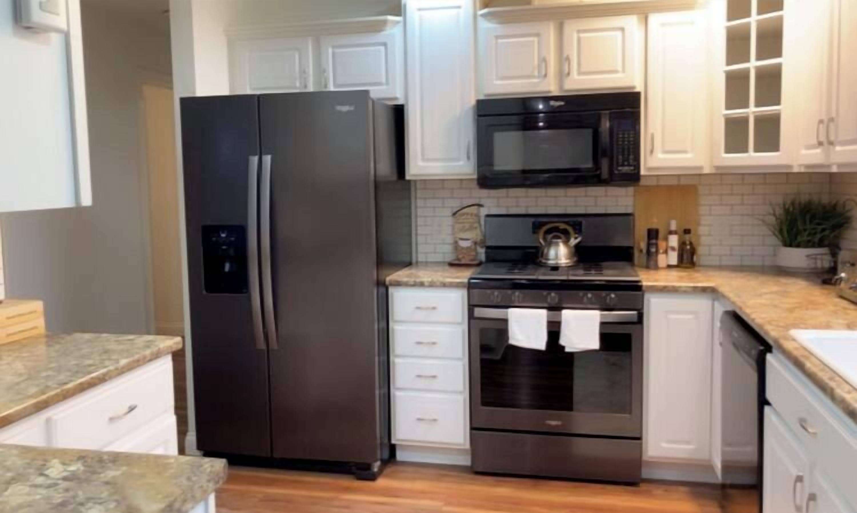 A modern kitchen with stainless steel appliances, white cabinetry, and a granite countertop.