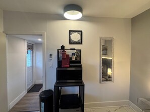 Un pasillo con una puerta, una mesita con un objeto rojo, una cita motivacional enmarcada y un espejo en la pared.