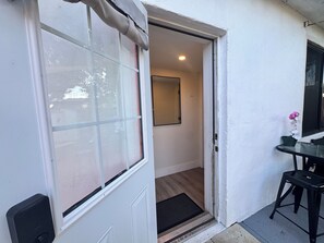 Una puerta que da a un cuarto con picaporte visible, una mesita con una silla y una planta en maceta.