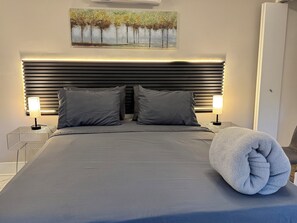 A modern bedroom with a large bed, two bedside lamps, a headboard with horizontal slats, and a painting above the bed.