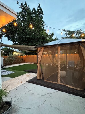 Un espace extérieur abrité avec des guirlandes lumineuses, une pelouse et une clôture en bois.