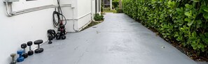 A concrete pathway leading to a building with a white exterior, a hedge on one side, and a row of dumbbells on the ground.