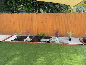 A garden area with a wooden fence, potted plants, and a tarp-covered planting bed.