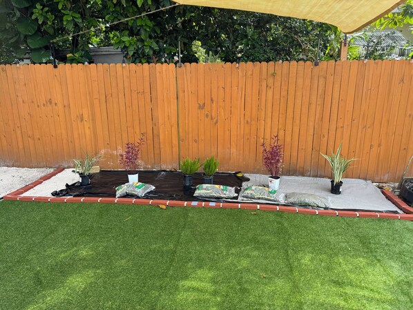 A garden area with a wooden fence, potted plants, and a tarp-covered planting bed.