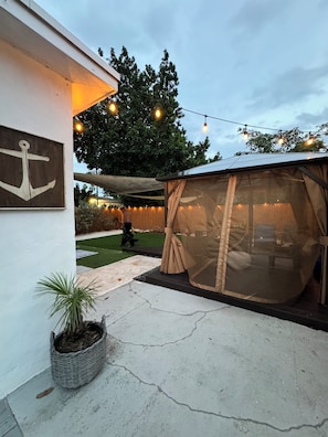 Un espacio al aire libre cubierto con una mesa, sillas, una planta en maceta y una guirnalda de luces.