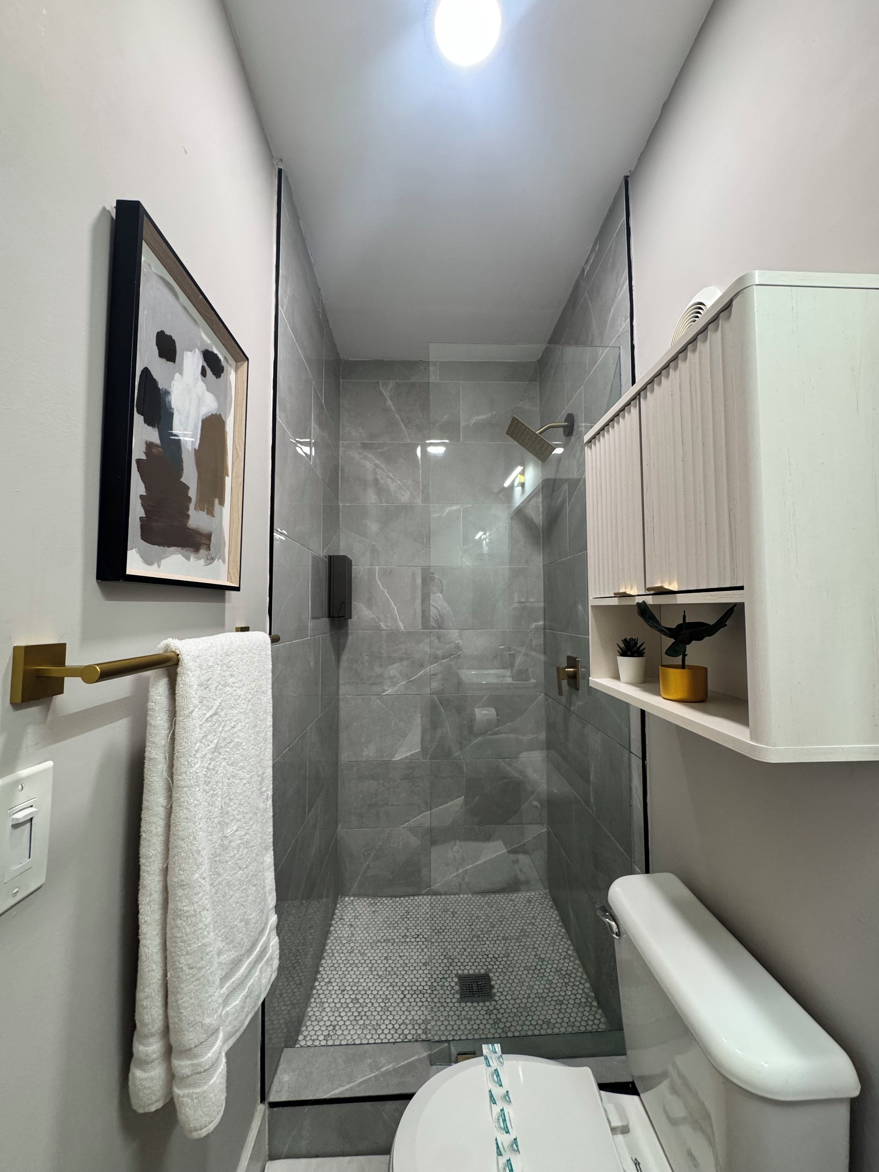 A modern bathroom with a glass-enclosed shower, a toilet, a sink, and a shelf with toiletries.