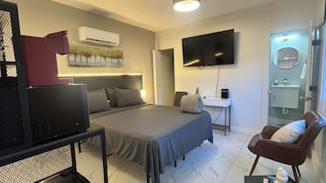 A hotel room with a bed, a desk, a television, a chair, and a bathroom.
