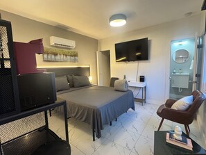 A hotel room with a bed, a desk, a television, a chair, and a bathroom.
