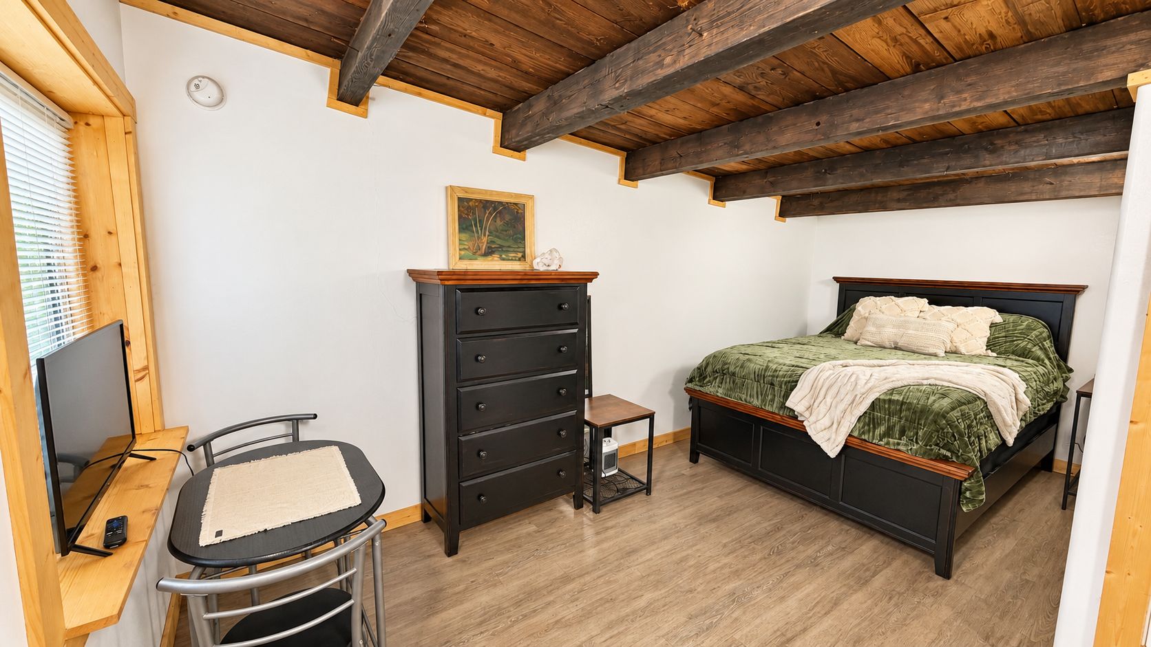 Un dormitorio con cama, tocador, escritorio, silla y un cuadro en la pared.