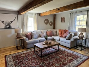 A living room with a sectional sofa, a coffee table, and a patterned rug. - Charming First Floor Farmhouse (Clarendon)