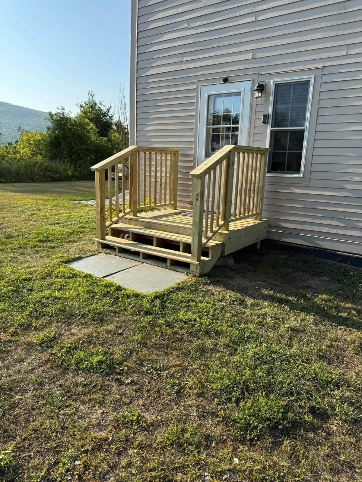 A wooden deck attached to a house with a window and a door.