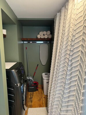 A laundry room with a washing machine, a drying rack, a broom, and a trash bin. - Charming First Floor Farmhouse (Clarendon)