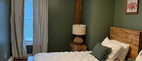 A bedroom with two beds, a nightstand with a lamp, a wooden headboard, and a window with curtains.