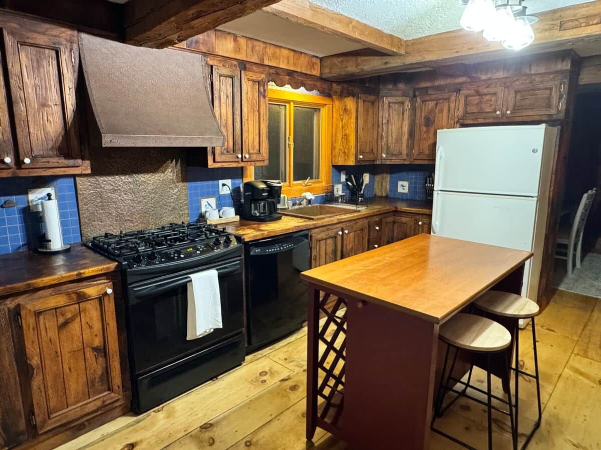 A kitchen with wooden cabinets, a black stove, a white refrigerator, and a wooden island with stools.