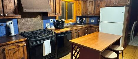 A kitchen with wooden cabinets, a black stove, a white refrigerator, and a wooden island with stools.