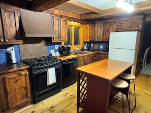 Una cocina con armarios de madera, una estufa negra, un refrigerador blanco y una isla de madera con taburetes.