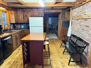 Eine Küche mit Holzausbau, einem weißen Kühlschrank, einem Holzesstisch mit Hocker und einer schwarzen Bank.