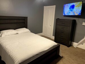 A bedroom with a bed, a dresser, a door, and a television on the wall.