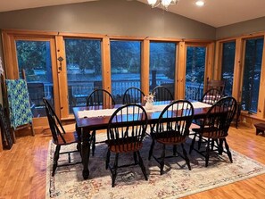 A dining area with a wooden table and chairs, large windows, and a view of a deck. - Reflections on the Lake (Hampton)