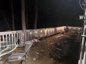 An outdoor patio area with metal chairs and tables, a wooden deck, and a railing. - Reflections on the Lake (Hampton)