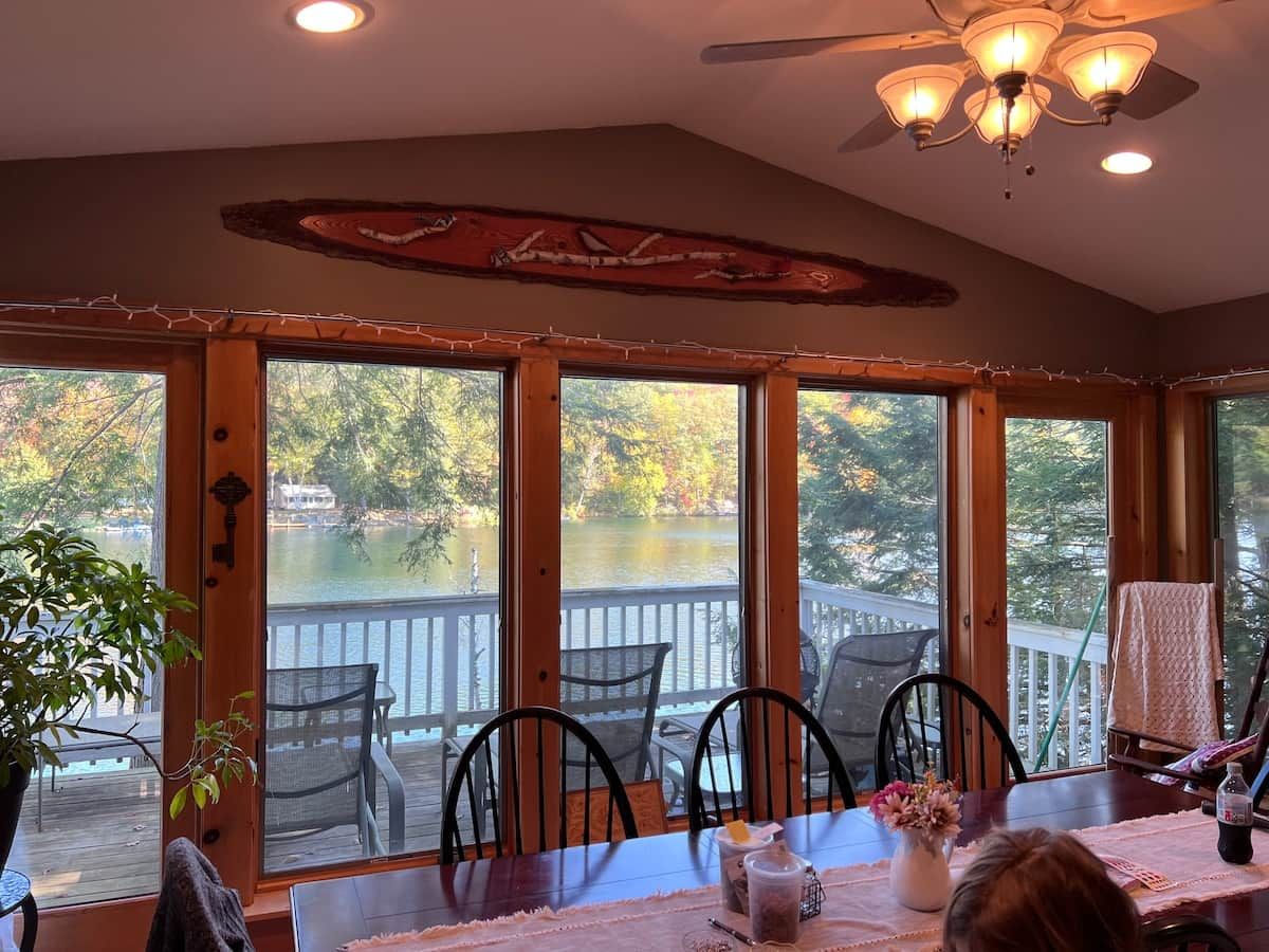 A dining area with a view of a lake, wooden deck, and a ceiling fan.
