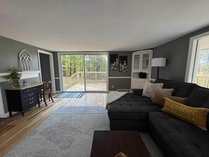 A living room with a dark sofa, a coffee table, and a dining area with a wooden cabinet and chairs. - Couple’s Retreat near Killington with Hot Tub (Mendon)