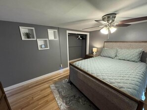 Ein Schlafzimmer mit Bett, Deckenventilator, Nachttisch und einer Tür zu einem Kleiderschrank.