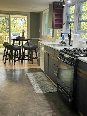 A kitchen with a central island, dark cabinetry, a stove, and a window overlooking a deck. - Couple’s Retreat near Killington with Hot Tub (Mendon)