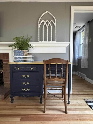 A room with a dark blue dresser with gold handles, a wooden chair, a white-framed window, and a plant on the dresser. - Couple’s Retreat near Killington with Hot Tub (Mendon)