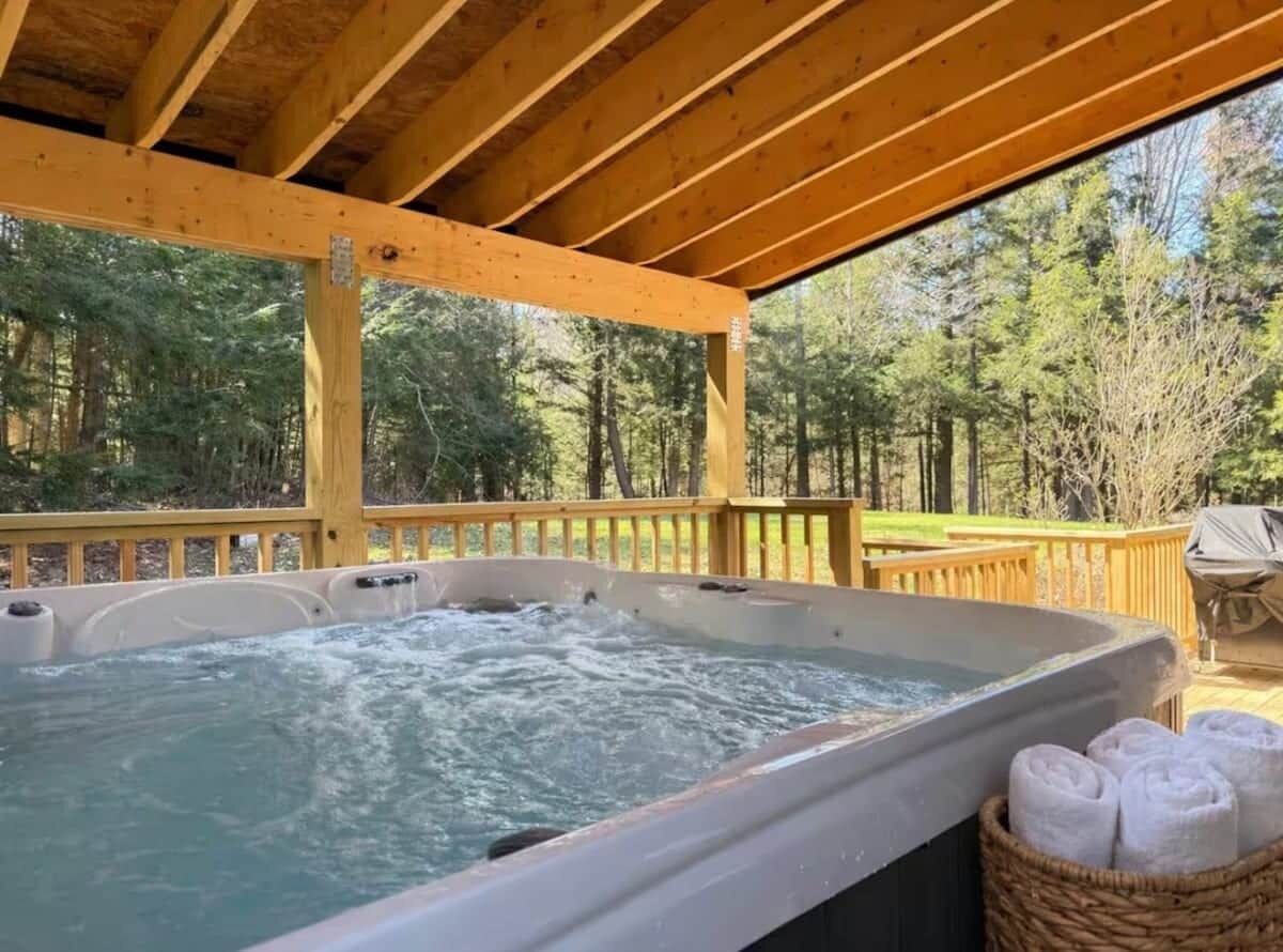 A hot tub under a wooden pergola with a view of a forested area.