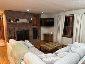 Ein Wohnzimmer mit Kamin aus Ziegelsteinen, einem Flachbildfernseher, einem Couchtisch aus Holz und einer Couch.